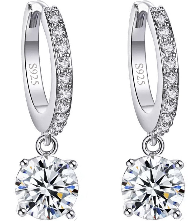 A pair of sterling silver huggie hoop earrings with a row of small clear stones and a large round clear gemstone dangling below, shown on a white background with inset quality marks.