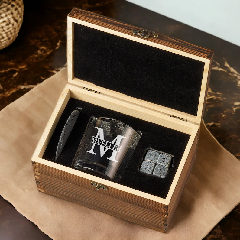 Open wooden gift box with velvet insert holding a whiskey glass, coaster and 4 whiskey stones