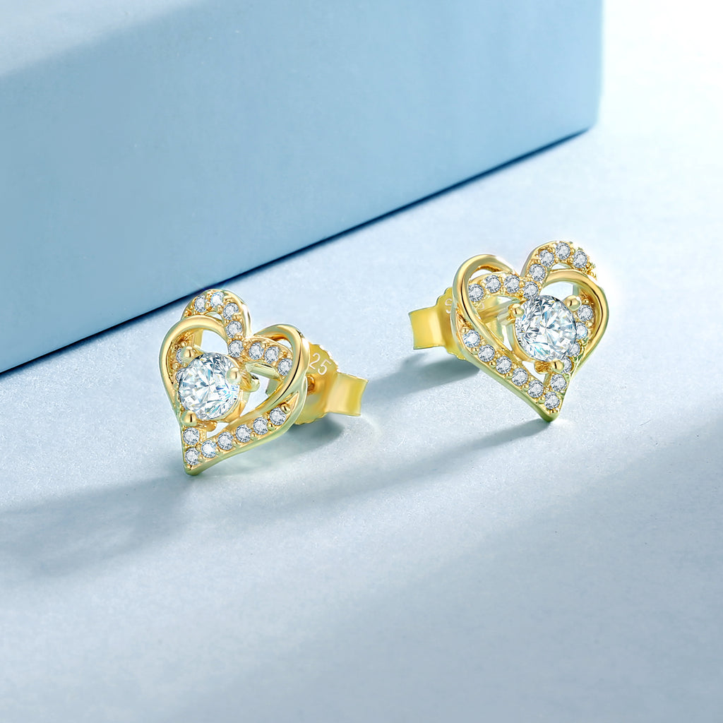 Pair of 14K gold plated heart moissanite studs on a pale blue background