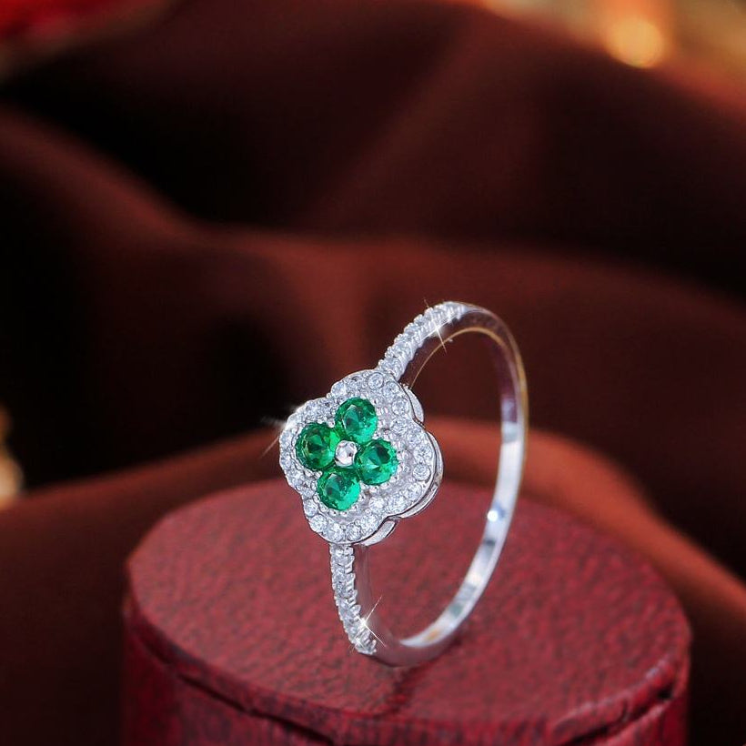 Sterling silver four leaf clover ring with green stones on a dark red jewelry box